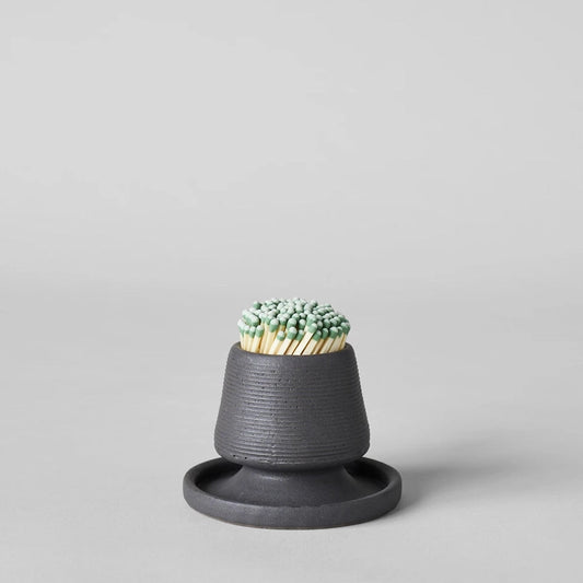 Black ceramic match holder with matches on a gray background. Handmade in the United States and looks lovely as a decorative item. Sold at Huset Shop on Abbot Kinney. 
