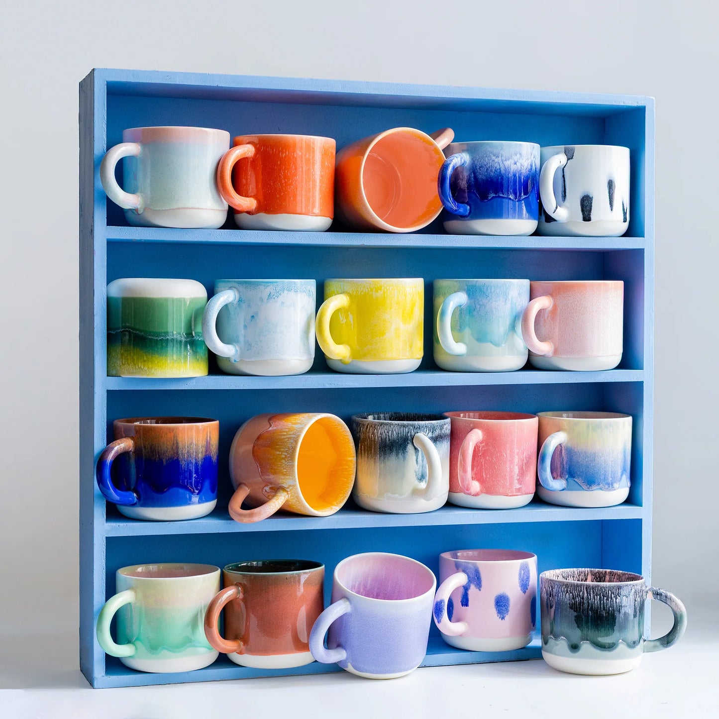 Collection of colorful mugs on a blue shelf against a light gray background