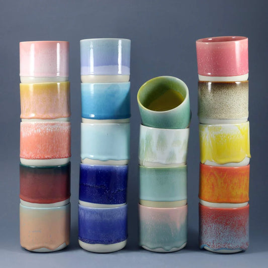 Set of colorful ceramic Studio Arhoj Quench Cup with layered glaze patterns on a gray background a rainbow of color and drippy ceramic glaze