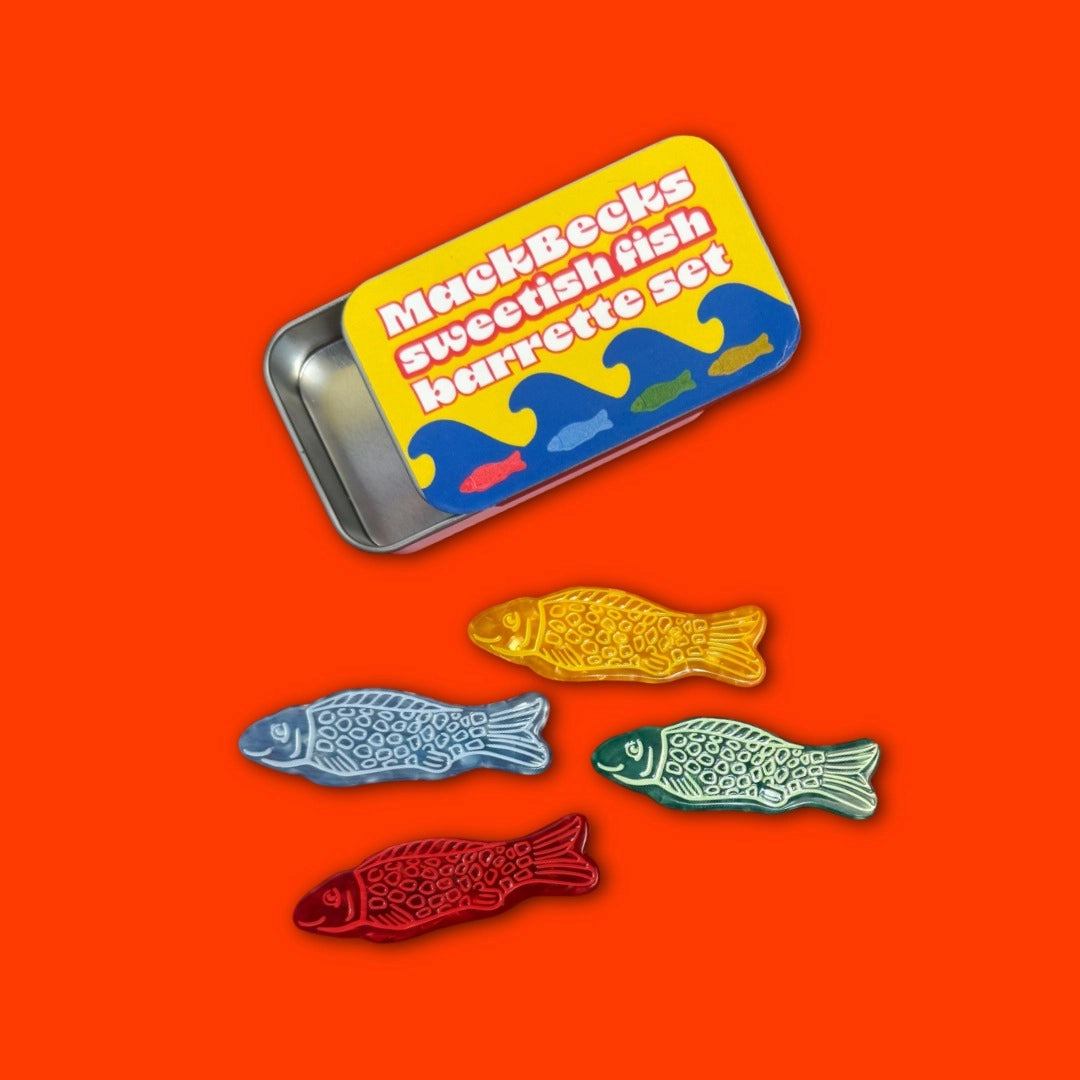 Set of colorful fish barrettes with a MuckBecks branded tin on an orange background