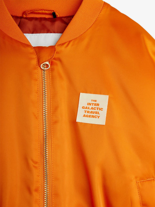 Orange jacket with a patch labeled 'The Inter Galactic Travel Agency' on a white background