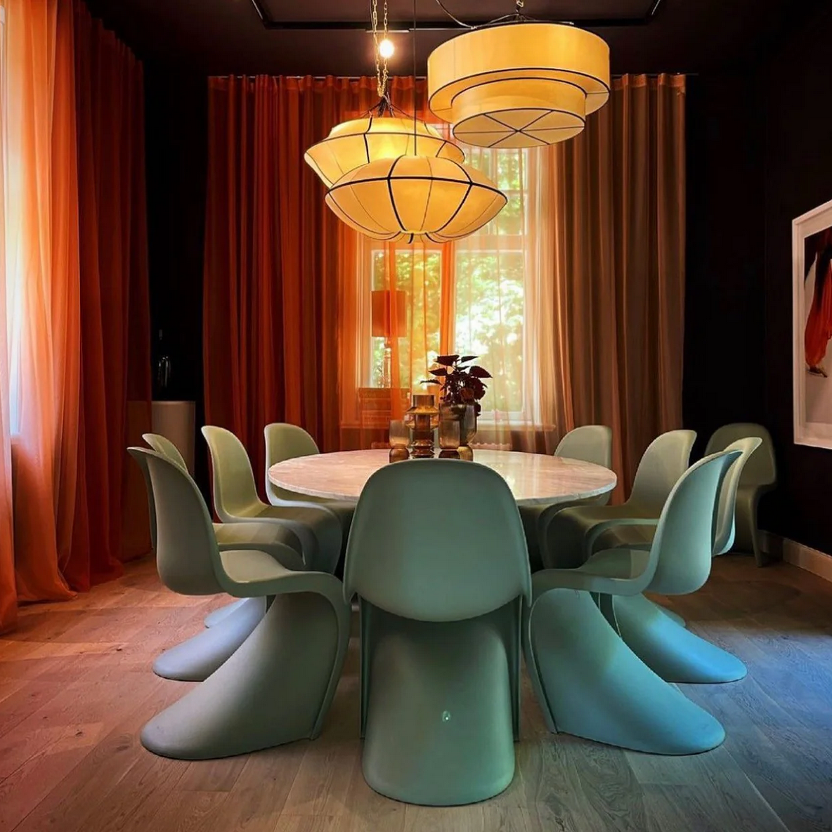 Modern dining room with round table and green chairs, illuminated by hanging lamps.
