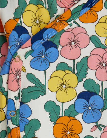 A close-up of a fabric product featuring a colorful pansy floral print on an off-white background. The pattern includes blue, pink, yellow, and orange flowers with green leaves, and a diagonal blue trim with white stitching.