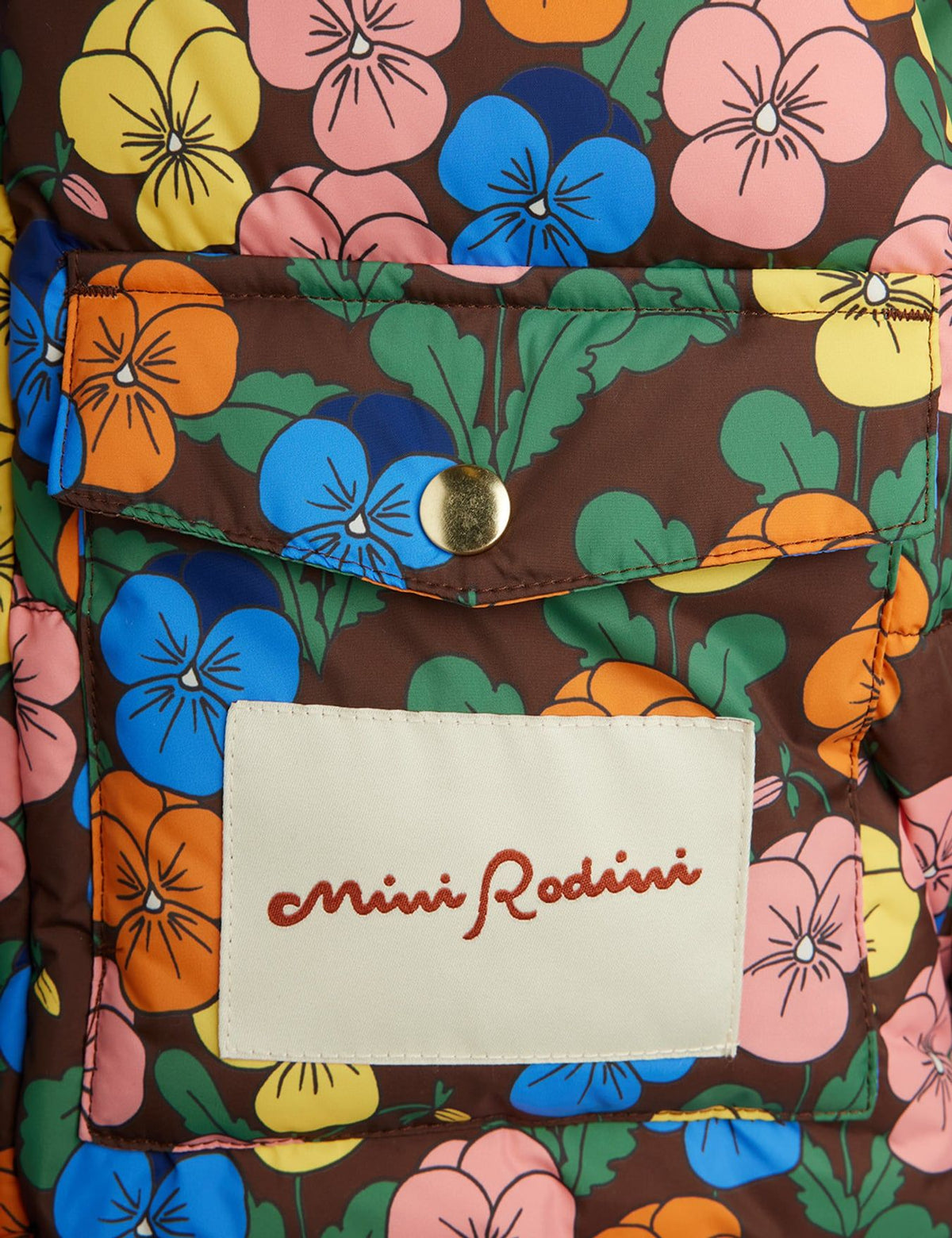 Close-up of a quilted puffer jacket featuring a brown base with a colorful floral print of pink, blue, orange, and yellow flowers. A white rectangular patch on the front pocket displays the 'Mini Rodini' brand name in red script.