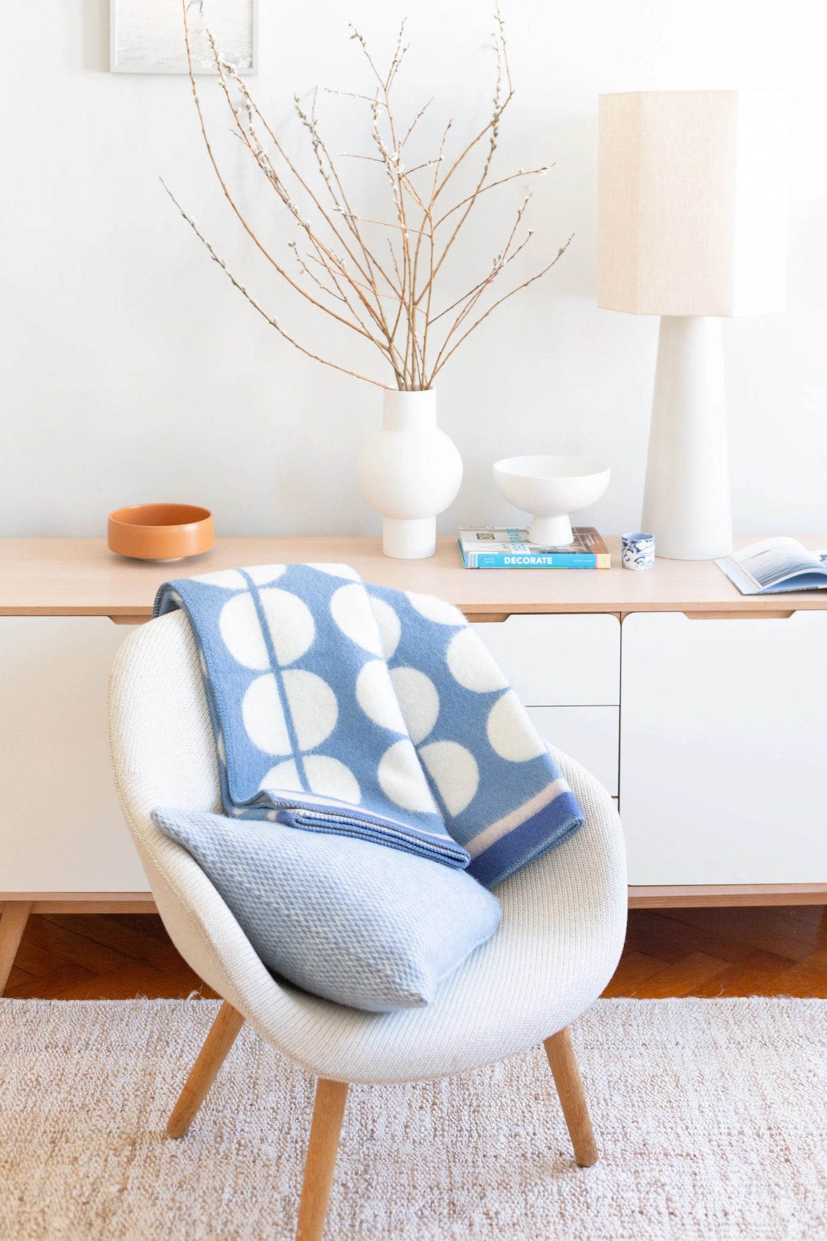 A light blue and white patterned throw blanket draped over a white armchair in a bright, modern room setting.
