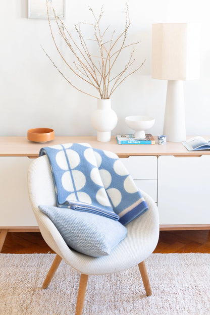 A light blue and white patterned throw blanket draped over a white armchair in a bright, modern room setting.