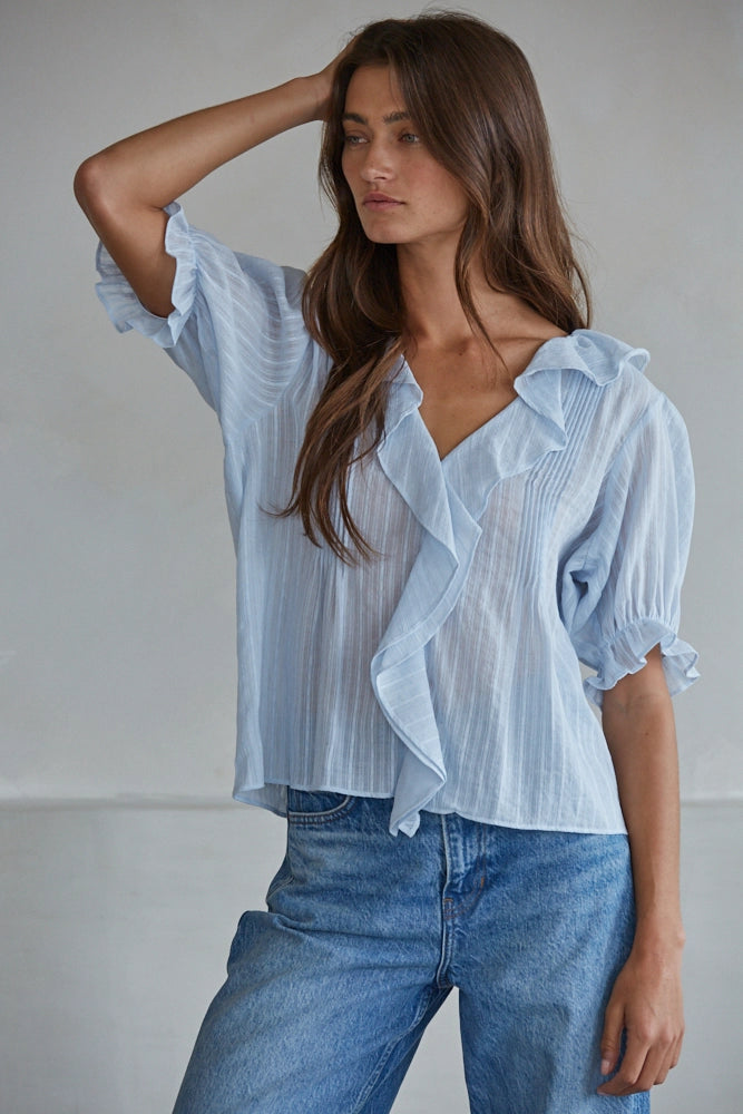 Woman wearing a light blue striped blouse and jeans against a plain background