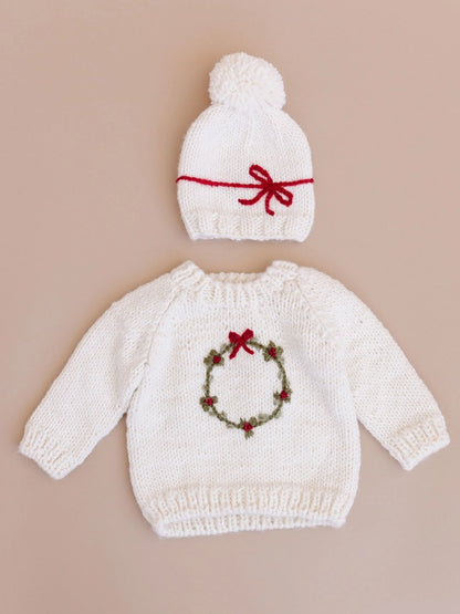 Deck the halls with our festive Wreath sweater. This Cream sweater features a hand-embroidered Moss wreath with Red berries and a simple bow. Pair with the Present hat&nbsp;