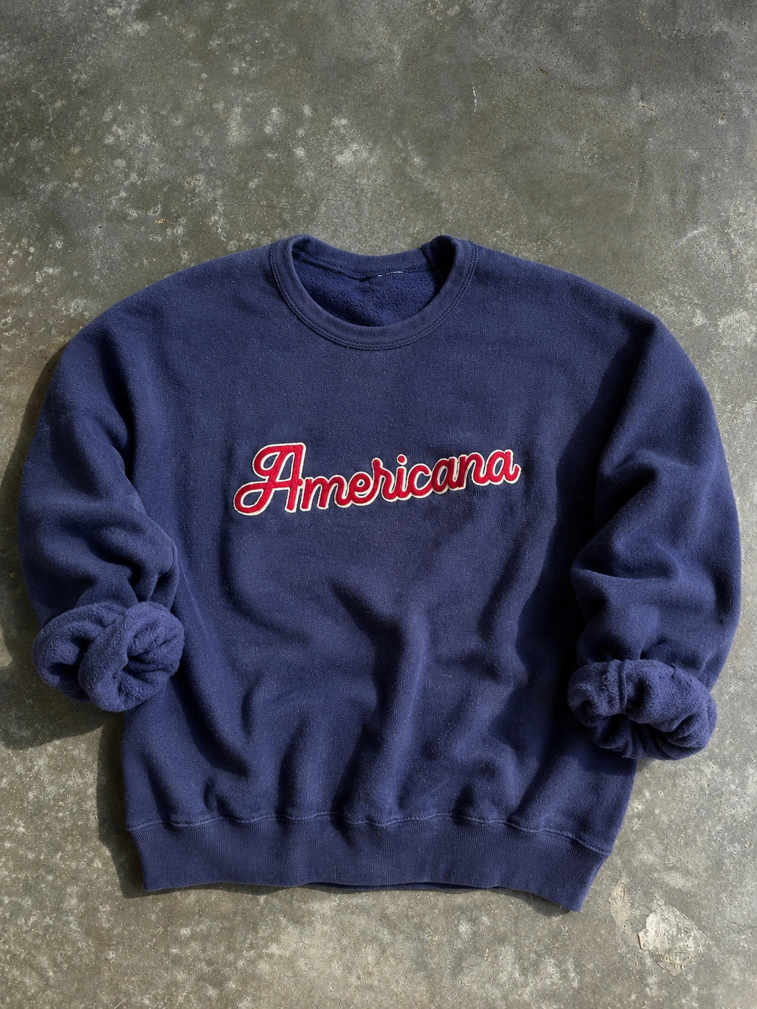 Navy blue sweatshirt with 'Americana' text on a concrete surface