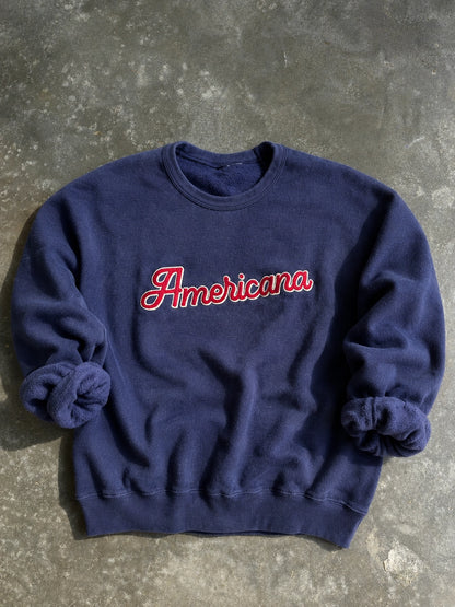 Navy blue sweatshirt with 'Americana' text on a concrete surface
