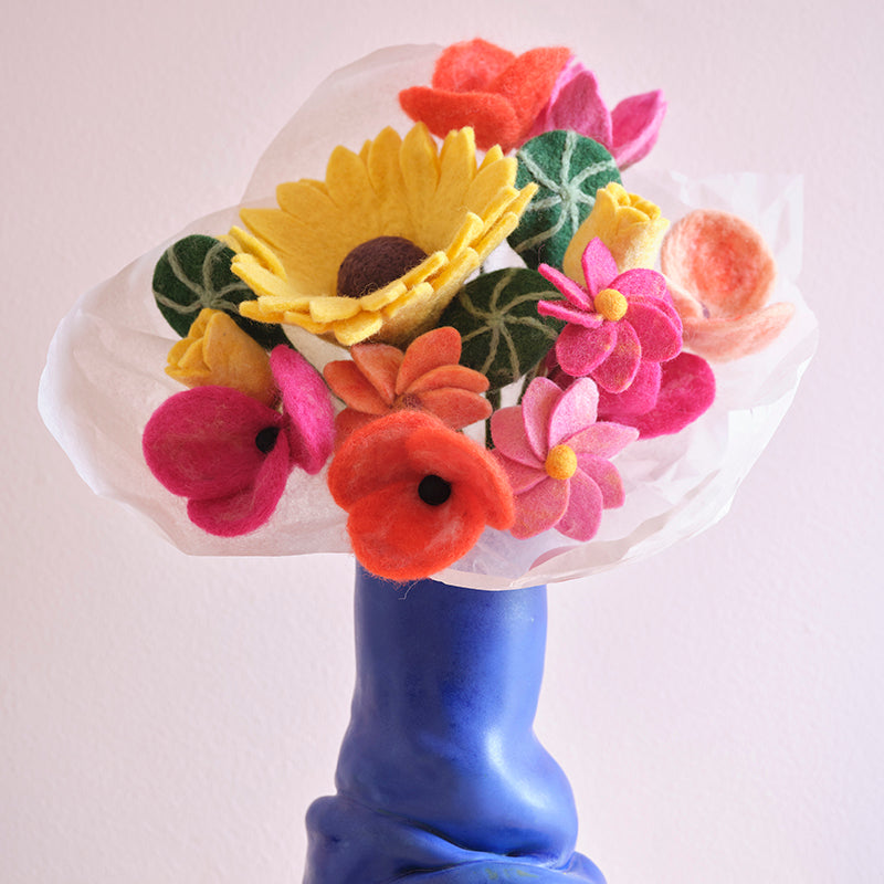 Aveva Wool Flower Bouquets that spark joy and will last you a lifetime. No more having to re buy flowers to fill the empty vases around your home, you can bring a touch of nature inside with colorful bouquets made with sustainable wool. This is the Amsterdam bouquet with a large sunflower and pink, yellow, and green hues in a blue vase.