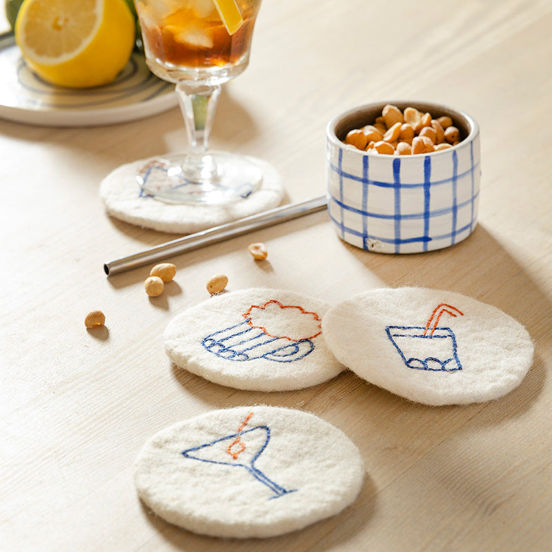 Set of embroidered coasters on a table with a glass of iced tea and snacks.