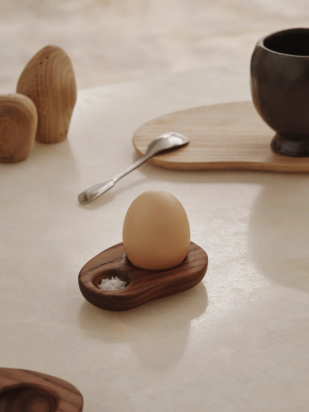 Egg on a wooden stand with salt, spoon, and cup on a light surface