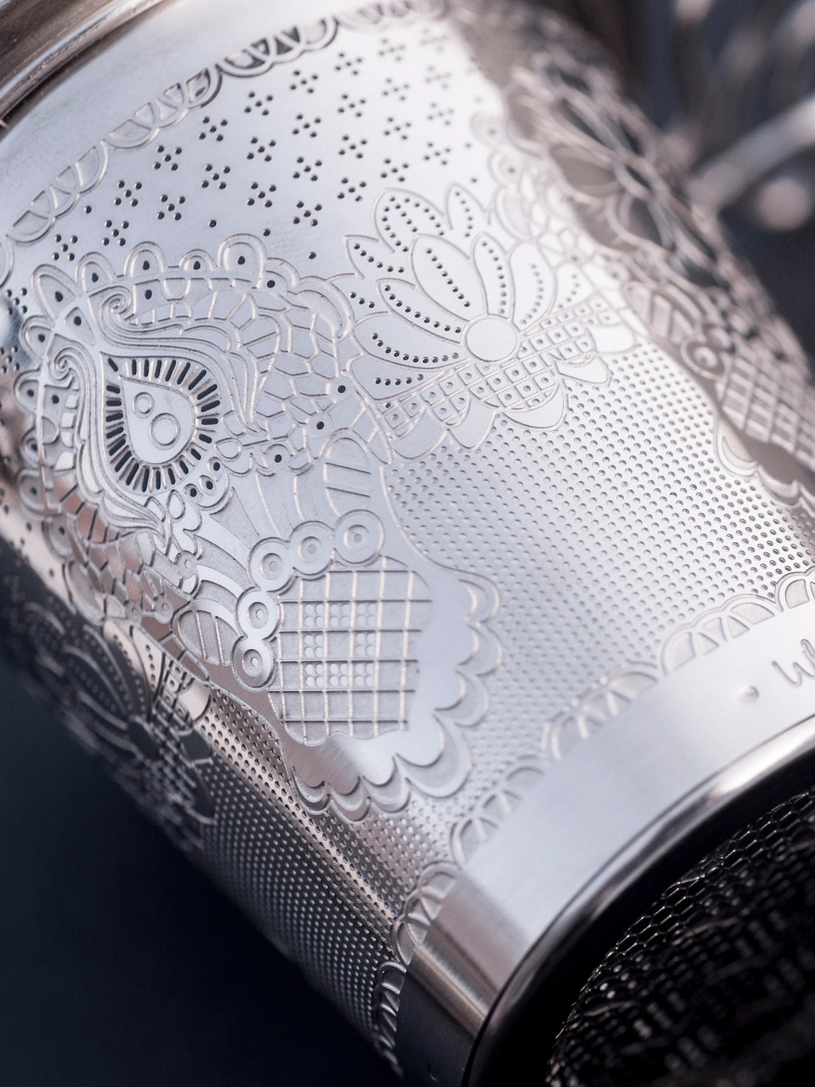 Silver tea infuser with intricate engravings on a dark background