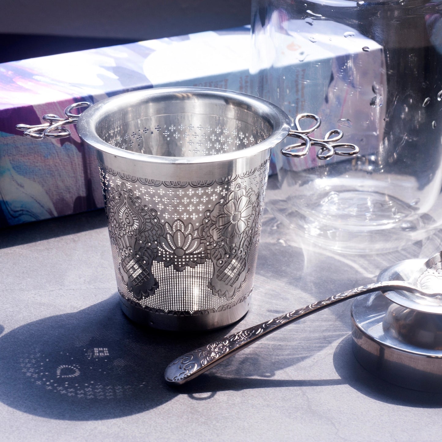 Silver tea strainer with intricate designs on a reflective surface