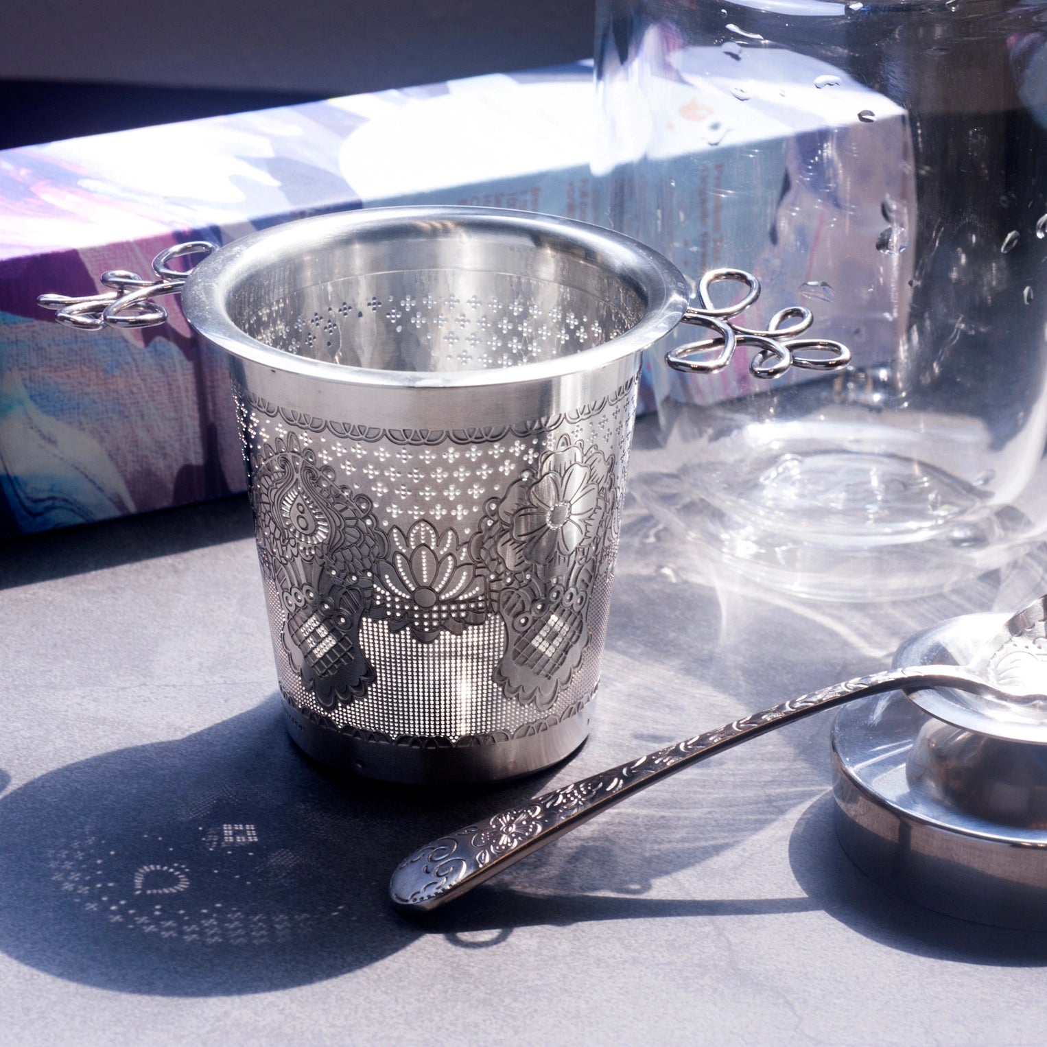 Silver tea strainer with intricate designs on a reflective surface