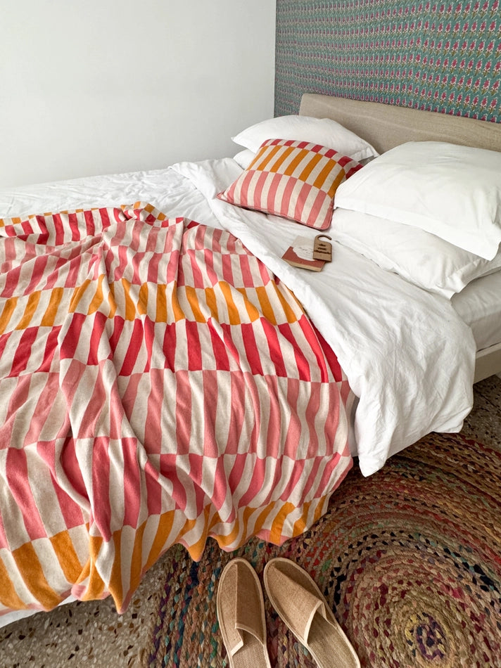 Bed with colorful striped bedding and white pillows, featuring a patterned rug.