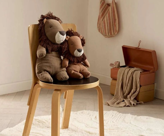 Two plush lion toys on a wooden chair in a room with a suitcase and blanket.