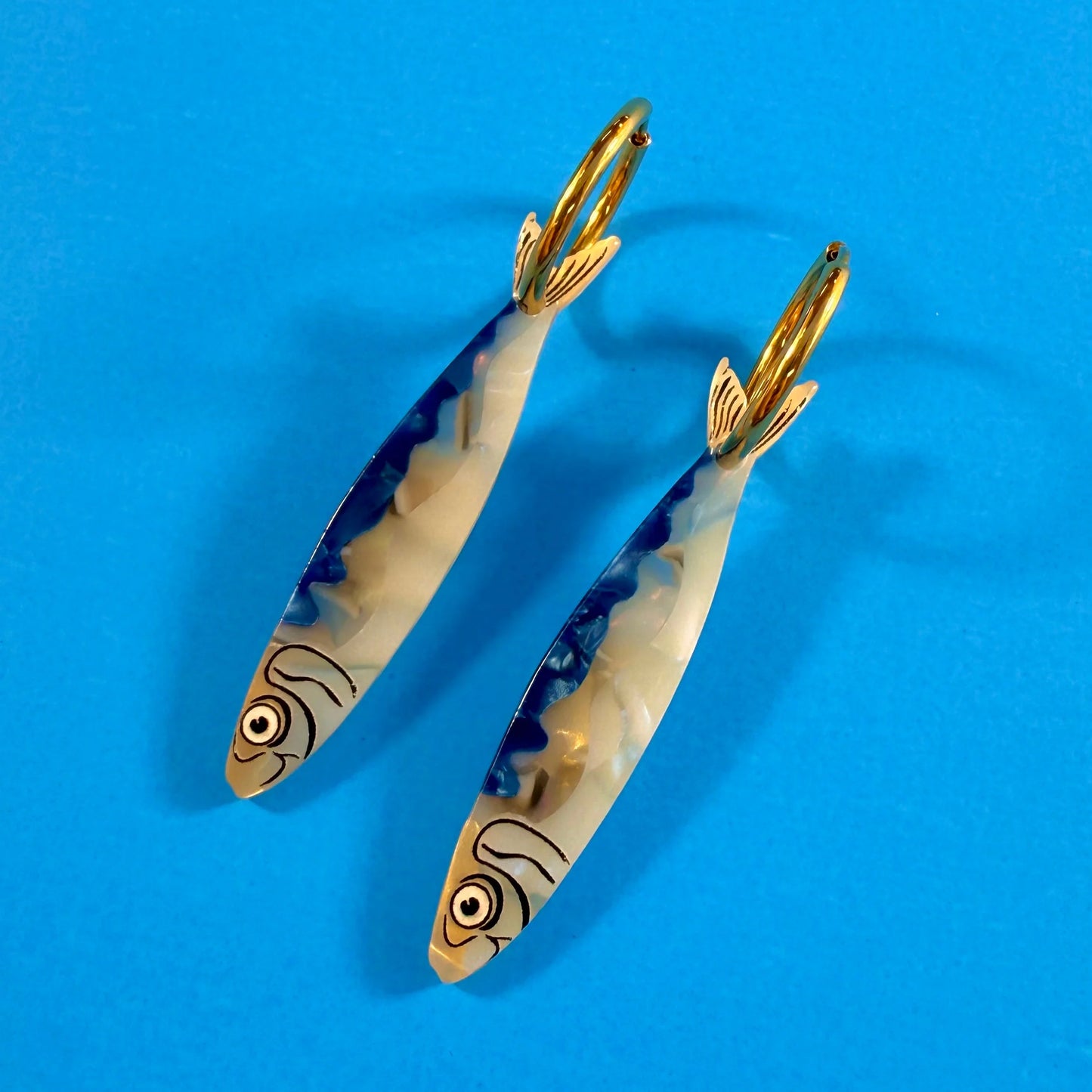 Two gold fish-shaped earrings on a blue background