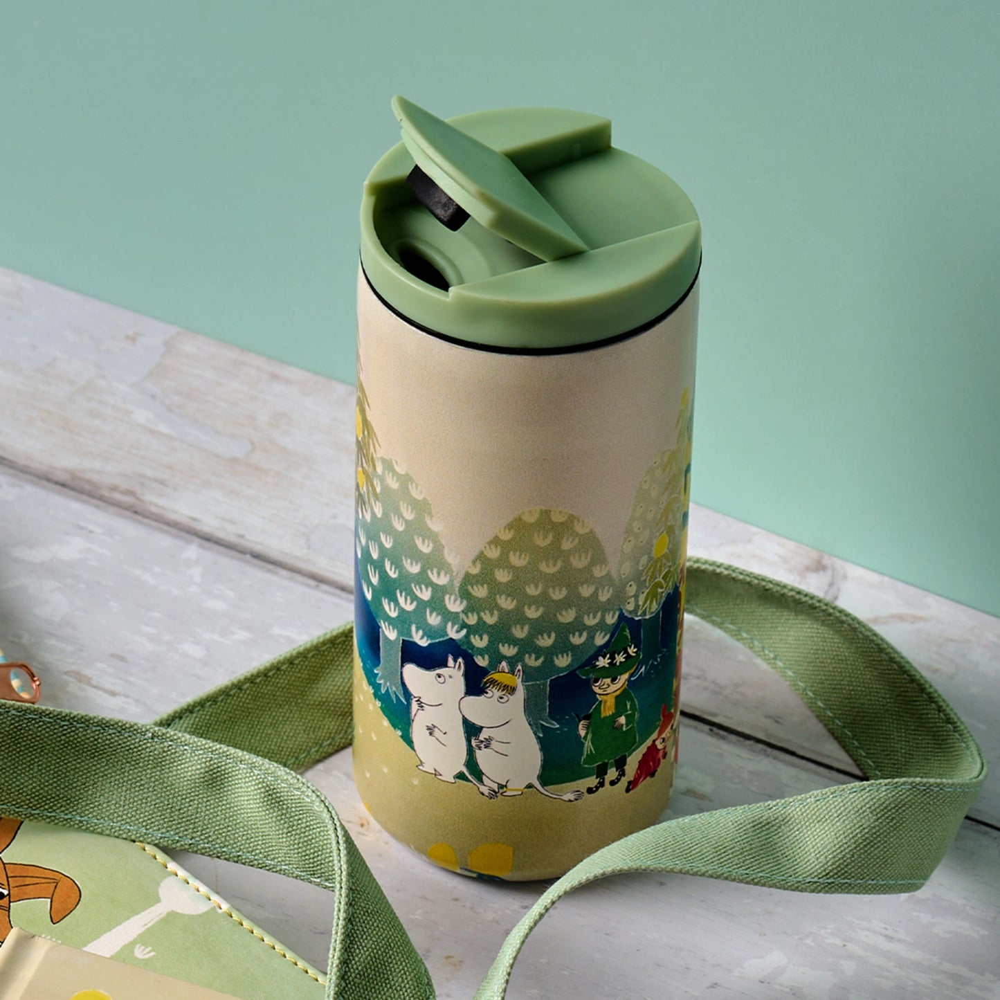 Green water bottle with a strap on a light wooden surface against a light green background
