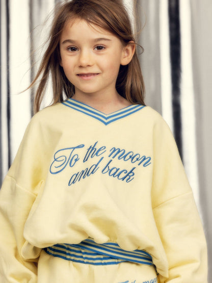 Young girl wearing a yellow sweatshirt with blue text against a neutral background