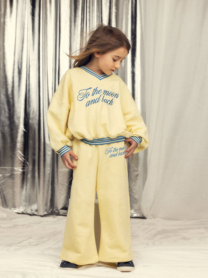 Person wearing a yellow outfit with text, standing against a silver curtain background