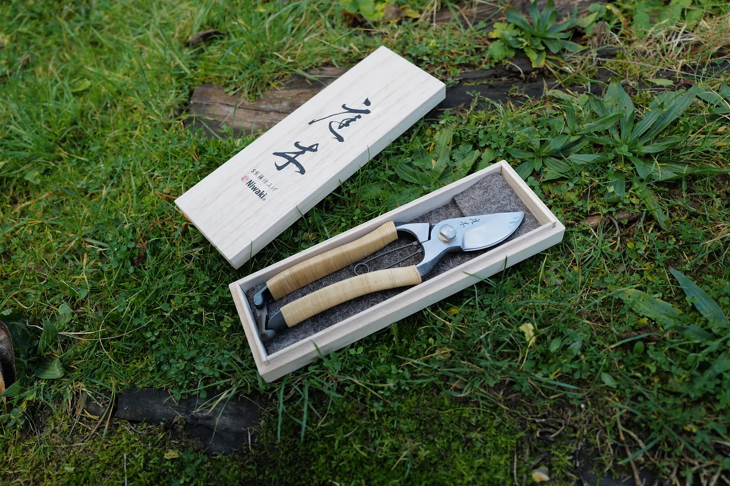 Gardening shears in a wooden box on grass. Limited production batches. Niwaki Secateurs are presented in a handmade Paulownia box. Known in Japan as Kiribako, these simple wooden boxes are used to store art and treasured objects.