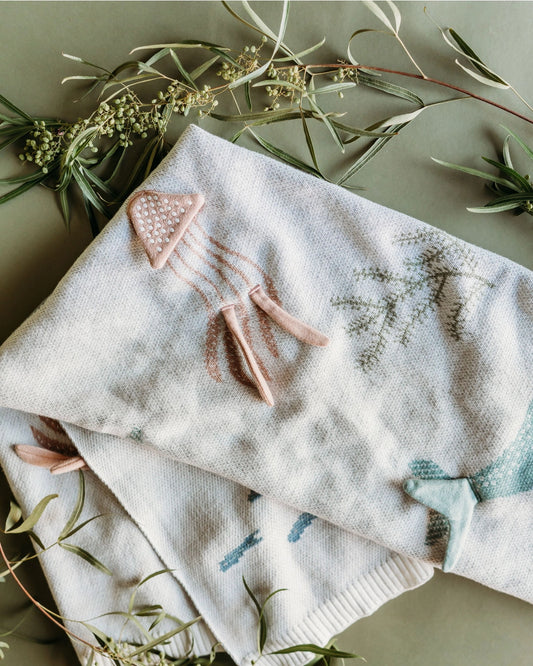 Embroidered fabric with floral patterns and a pink clip on a light background with greenery.