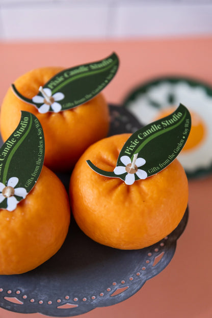 Three tangerines with decorative labels on a black stand against a pink background
