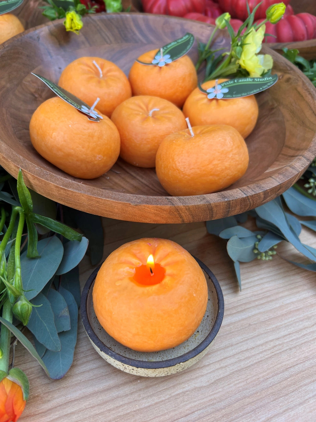 Wooden bowl with orange candle-like items and a lit candle on a wooden surface.