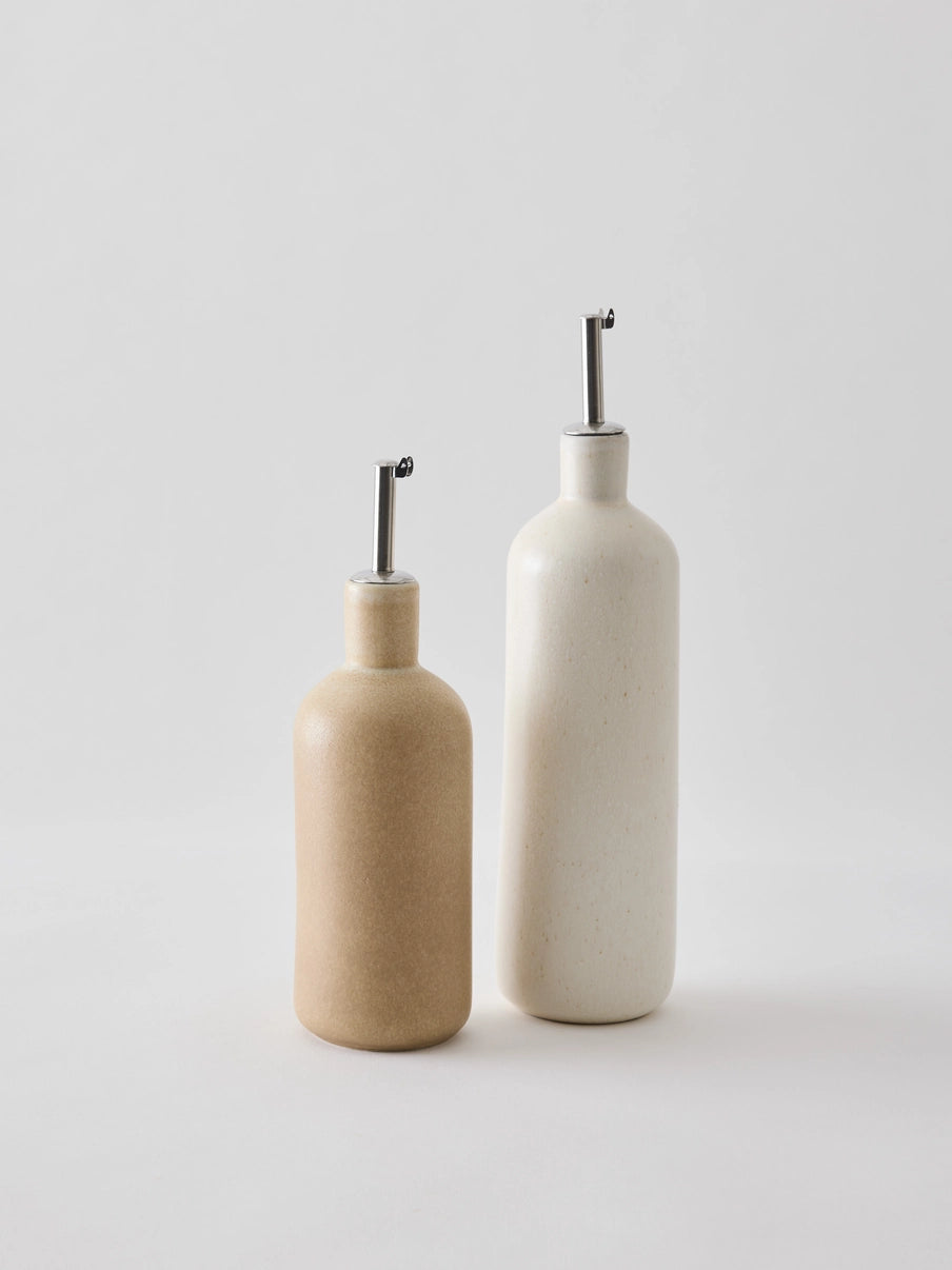 Oil bottle in cream-coloured stoneware with a narrow metal spout that provides a smooth and controlled flow. The spout is fitted with a silicone cork to ensure an airtight seal when pouring. Perfect for oil, vinegar, or other liquid condiments in the kitchen. Available in two sizes and part of the Palermo stoneware series. Swedish design from Tell Me More and sold at Huset Shop in Venice Beach. The Scandinavian homeware fits any aesthetic. 