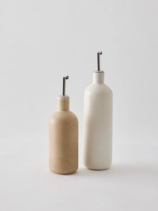 Oil bottle in cream-coloured stoneware with a narrow metal spout that provides a smooth and controlled flow. The spout is fitted with a silicone cork to ensure an airtight seal when pouring. Perfect for oil, vinegar, or other liquid condiments in the kitchen. Available in two sizes and part of the Palermo stoneware series. Swedish design from Tell Me More and sold at Huset Shop in Venice Beach. The Scandinavian homeware fits any aesthetic. 