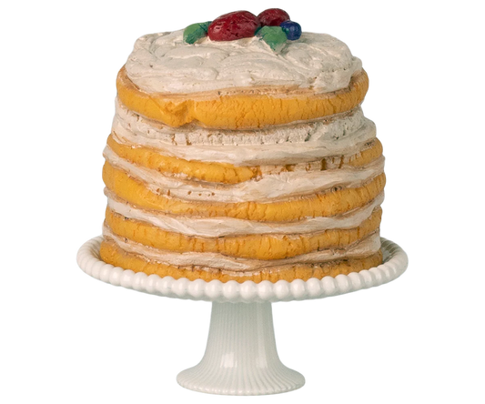 Layered cake with white frosting and fruit on top, placed on a white cake stand.
