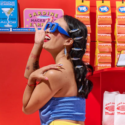 Woman wearing blue sunglasses and a blue top in front of a red wall with product displays.