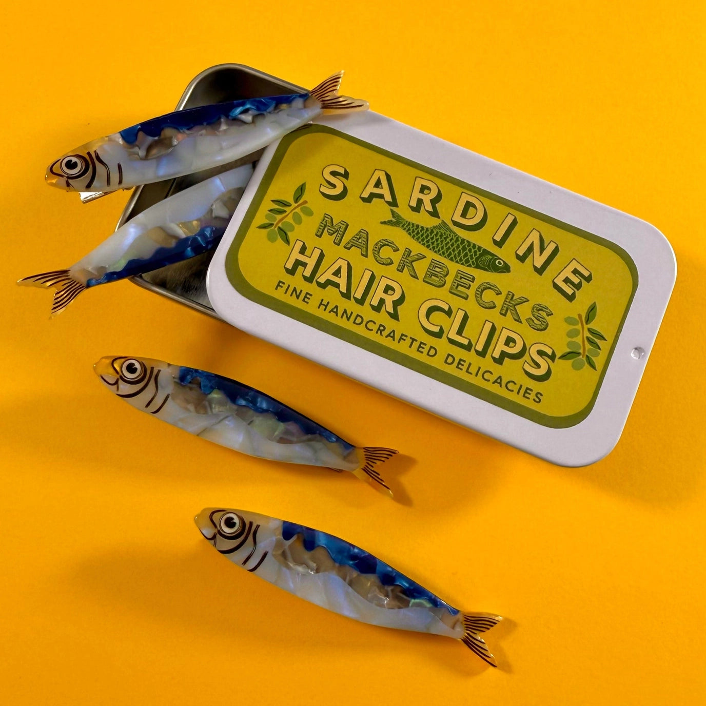 Sardine-shaped hair clips with a tin labeled 'Mackbecks Hair Clips' on a yellow background