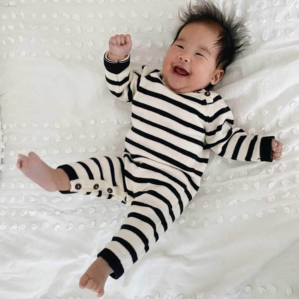 Baby wearing a black and white striped onesie on a white textured surface