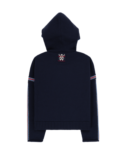 Two women sitting in a snowy landscape, wearing embroidered clothing, a true tribute to Norwegian heritage. This hooded sweater is crafted from 100% Norwegian wool, sourced from free-ranging sheep, and features embroidered motifs inspired by the traditional Norwegian Bunad of Telemark, Hallingdal, and Gudbrandsdalen.