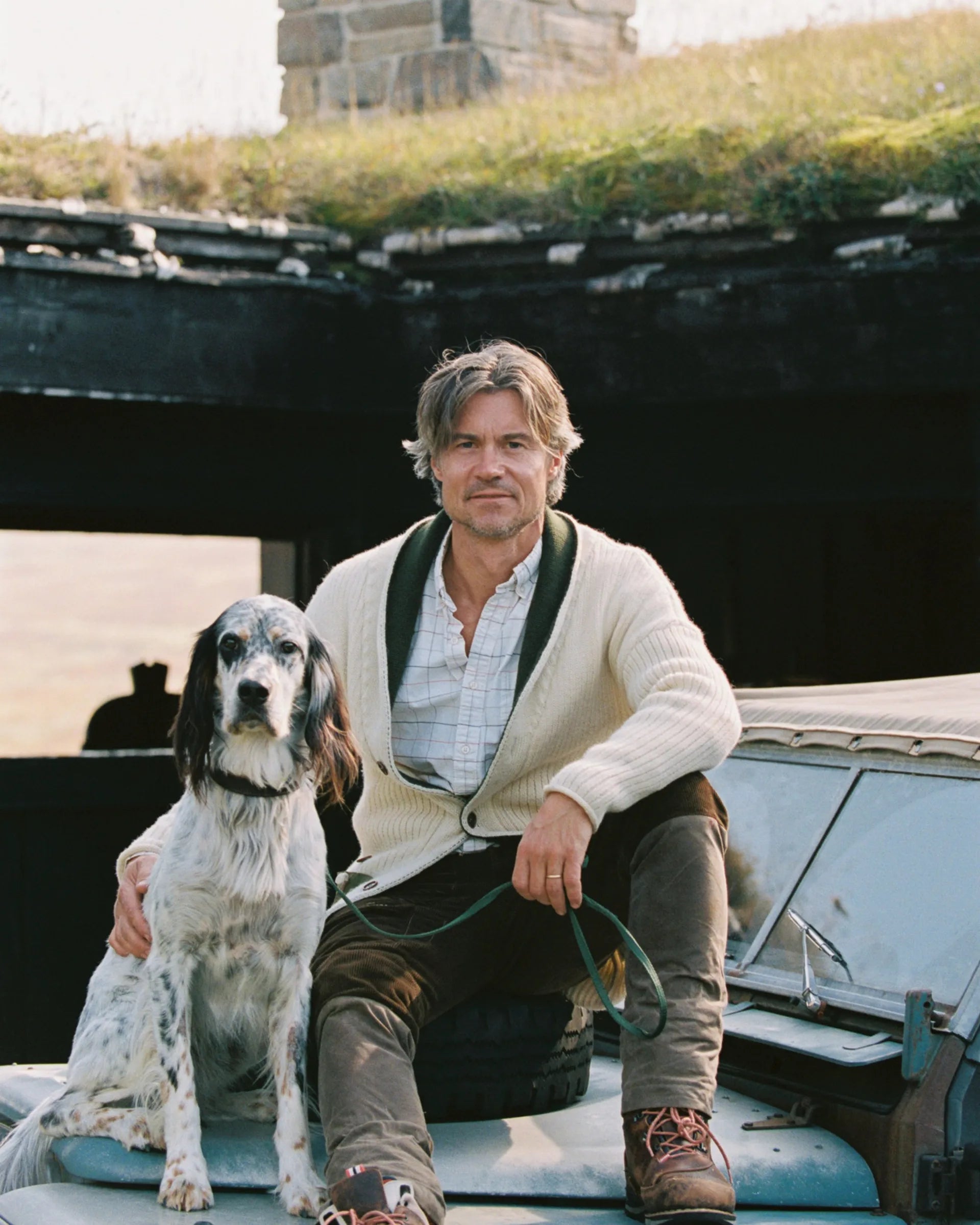 Handsome man in a the new norwegian brand sweater and cardigan standing next to a dog on an old Land Rover in a rustic setting. The cozy nature of this sweater is perfect for fall 2025 and men's fashion. Amundsen Sports, scandinavian, los angeles, venice beach, Huset shop, gift shop and shopping for men and women, dogs, and kids