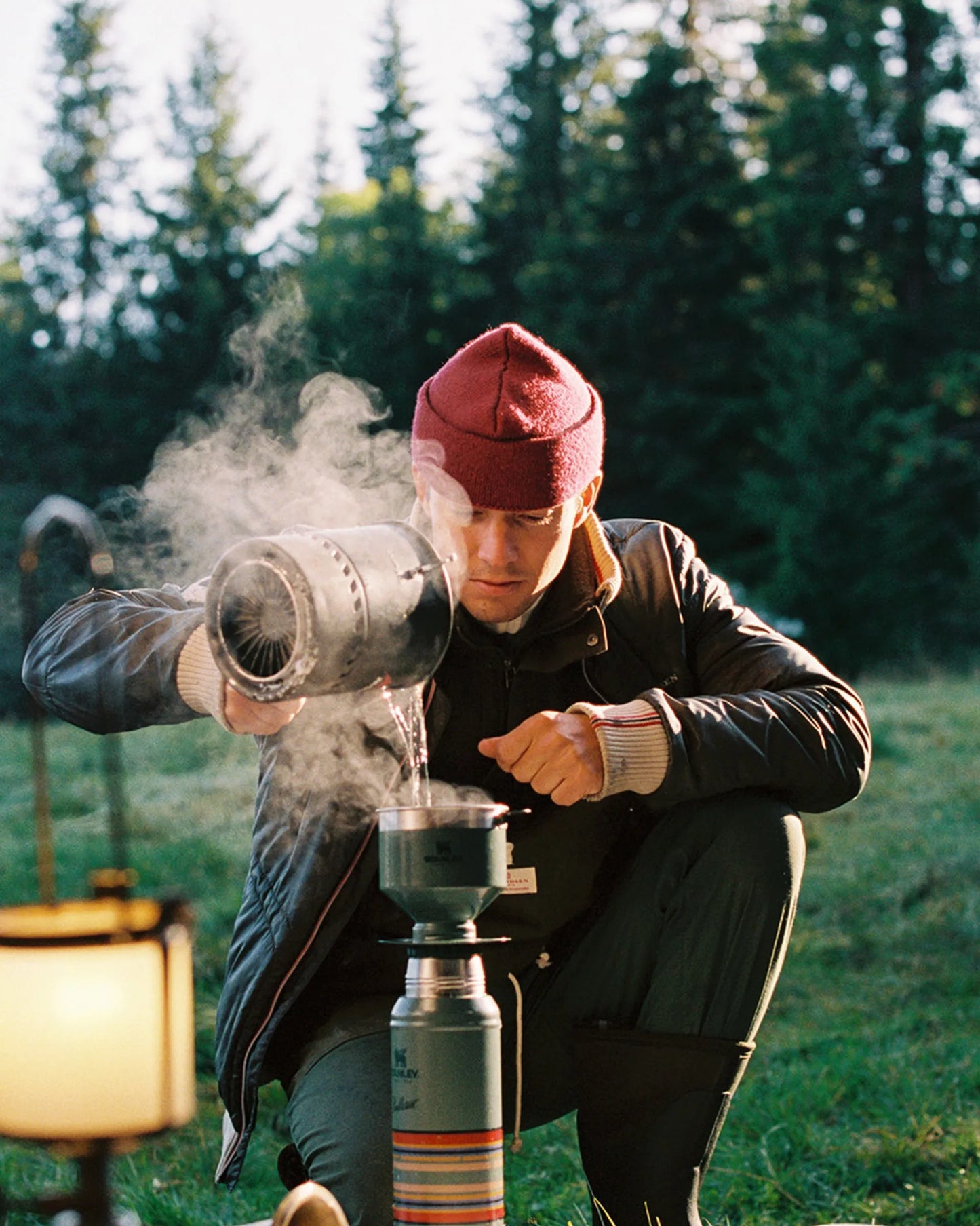 Norwegian camping or hiking, or anything involving the outdoors you will love this jacket. Lightweight durable polyamide face, 120 grams Norwegian Woolinside insulation, Cuffs, waist and neck knitted in pure merino wool, Antarctic Tartan lining
Amundsen Peak patches on upper sleeves. He is using a camping stove to make some coffee surrounded by trees.