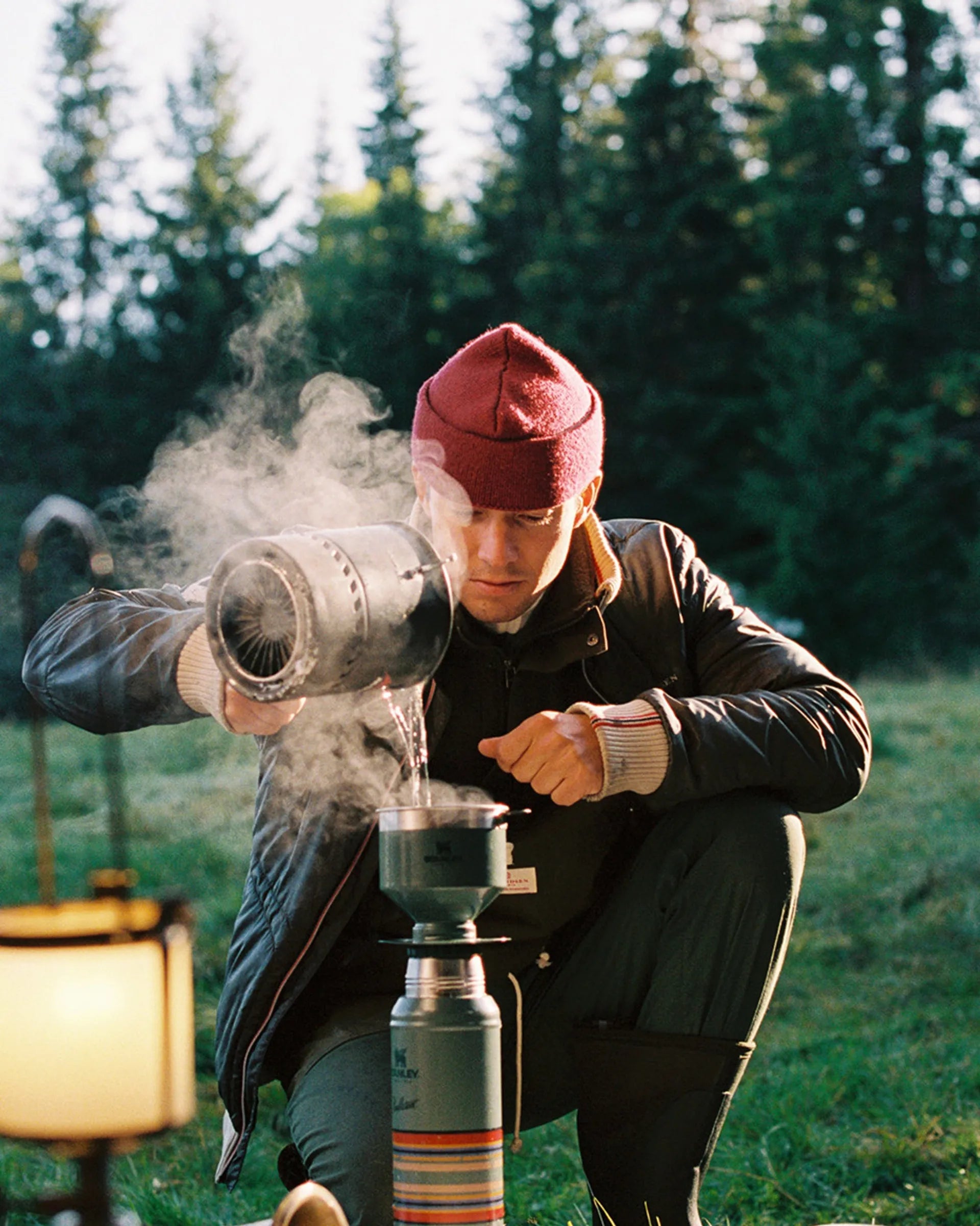 Norwegian camping or hiking, or anything involving the outdoors you will love this jacket. Lightweight durable polyamide face, 120 grams Norwegian Woolinside insulation, Cuffs, waist and neck knitted in pure merino wool, Antarctic Tartan lining
Amundsen Peak patches on upper sleeves. He is using a camping stove to make some coffee surrounded by trees.