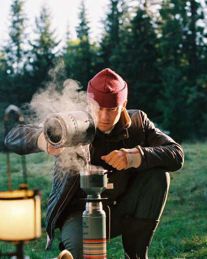 Norwegian camping or hiking, or anything involving the outdoors you will love this jacket. Lightweight durable polyamide face, 120 grams Norwegian Woolinside insulation, Cuffs, waist and neck knitted in pure merino wool, Antarctic Tartan lining
Amundsen Peak patches on upper sleeves. He is using a camping stove to make some coffee surrounded by trees.