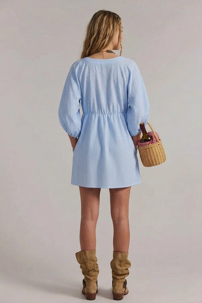 Woman wearing a light blue dress holding a woven basket against a plain background